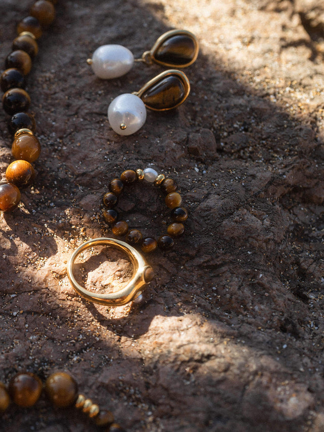 Goldring und Ohrringe mit Tigerauge, Perlenarmband auf dunklem Stein, PURELEI Eleganz.