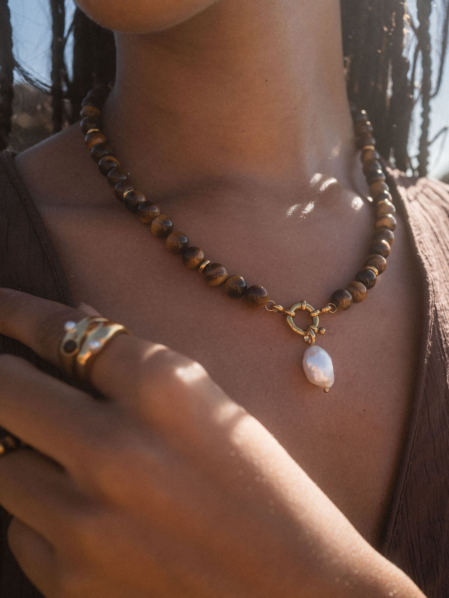 Braune Perlenkette mit Muschel-Anhänger, getragen von PURELEI, strahlt natürliche Eleganz aus.