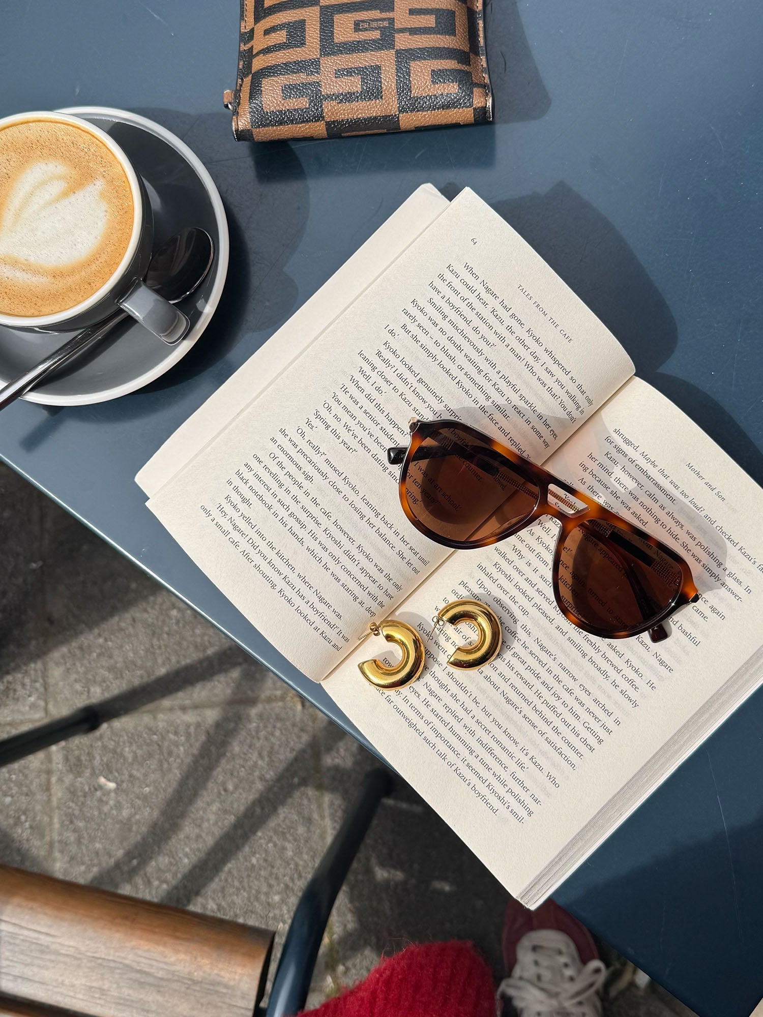 Palm Beach Sonnenbrille von PURELEI in braunem Schildpatt mit goldenen Bügeln auf offenem Buch, warme Sommerstimmung.