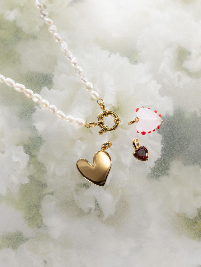 Heart Of Glass Charm von PURELEI, rosafarbenes Glasherz mit roten Punkten und goldener Fassung, elegant und feminin.