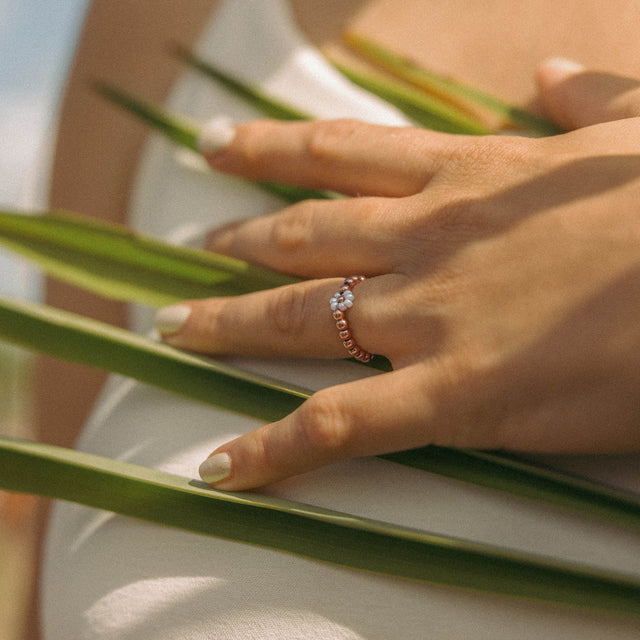 Roségoldener Ring mit Perlen, getragen auf einer Hand, umgeben von grünen Blättern – PURELEI.
