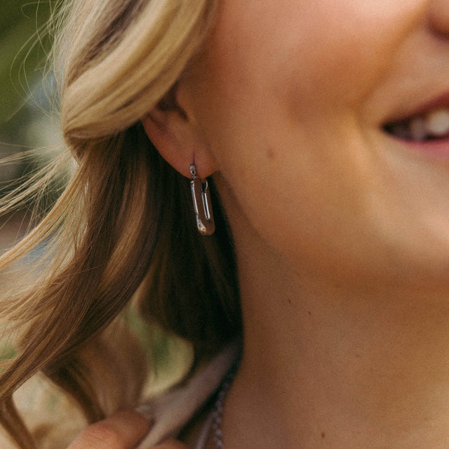 Silberne Ohrringe im modernen Design, getragen von einer lächelnden Frau, PURELEI.