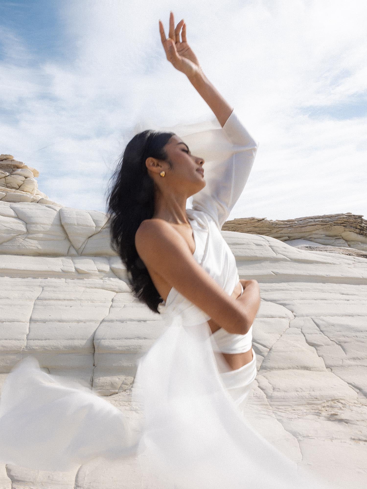 PURELEI Aries Letter Charm in glänzendem Gold, feines Design getragen vor heller Felslandschaft, elegant und feminin