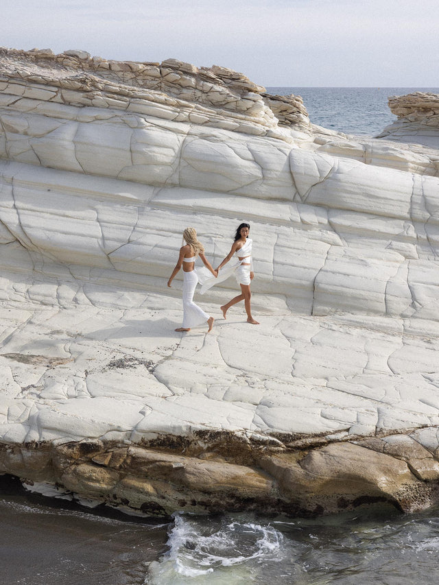 Cancer Letter Charm aus goldfarbenem Edelstahl, modern gestaltet, auf hellem Felsstrand mit Meeresblick, PURELEI.