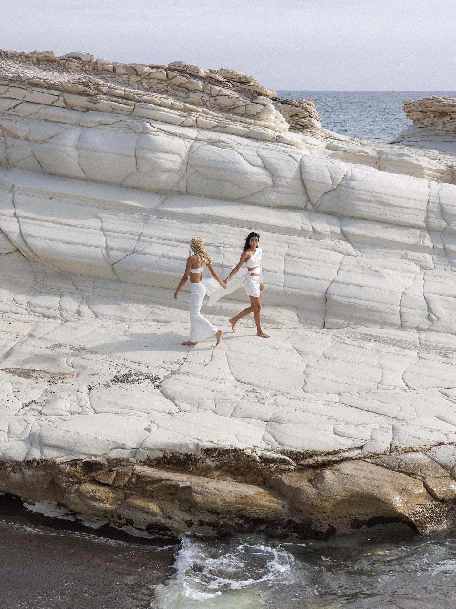 Sagittarius Letter Charm aus 18K Gold mit feiner Schrift, elegant und feminin vor heller Felskulisse von PURELEI