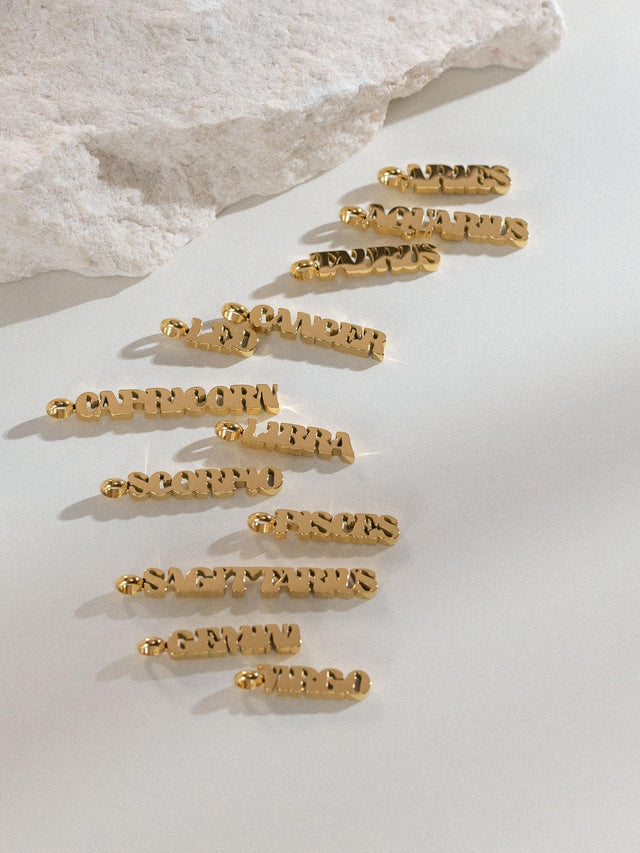 Goldener Aries Letter Charm aus Edelstahl, edel vergoldet, minimalistisch auf hellem Hintergrund, PURELEI.