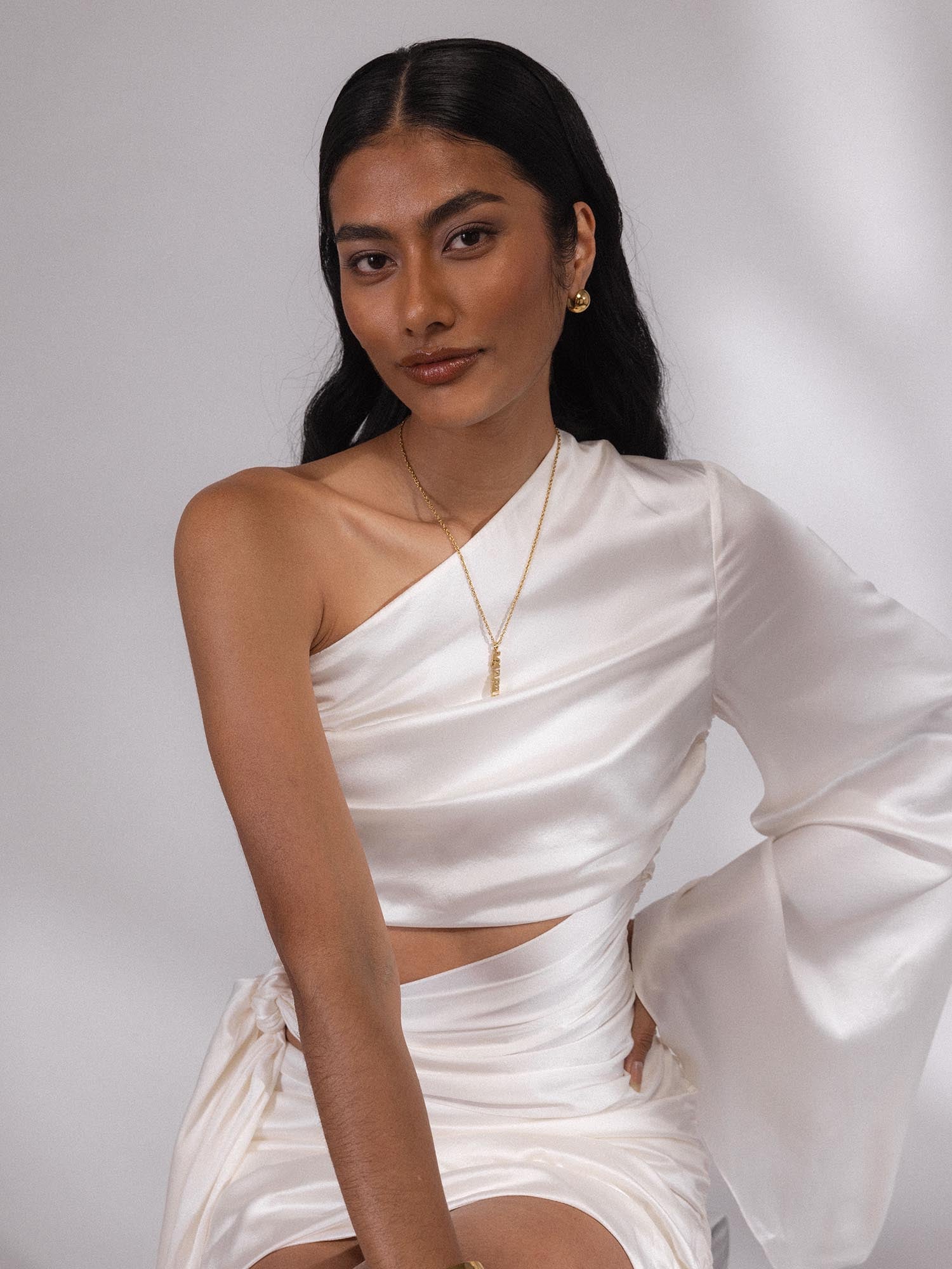 Goldener PURELEI Aquarius Letter Charm an filigraner Kette, elegant getragen zu weißem Satinoutfit, feminin und modern.