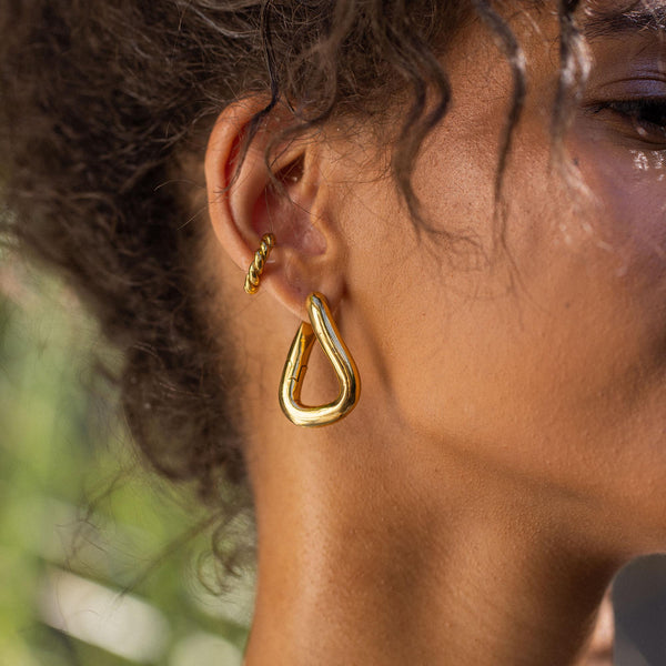 Goldene PURELEI Ohrringe in tropischer Form, elegant und modern, getragen in natürlicher Umgebung.