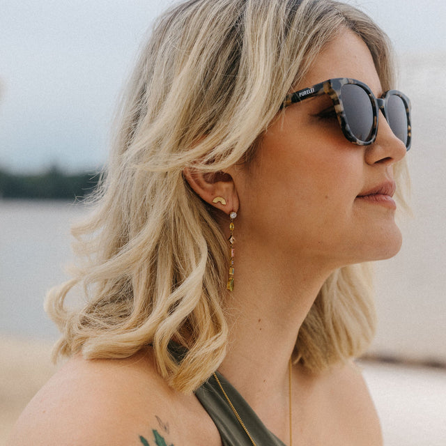 Goldene Ohrringe mit Regenbogen-Design, getragen von einer Frau am Strand – PURELEI.