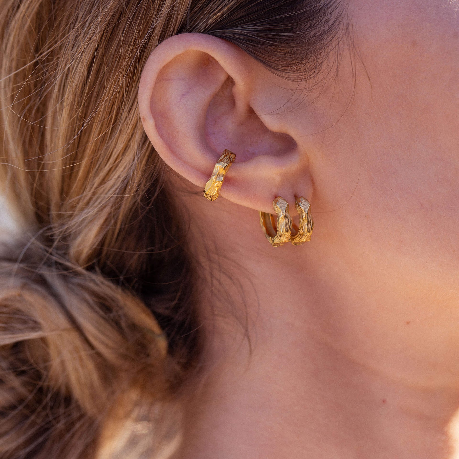 Goldene Creolen mit organischer Struktur, getragen am Ohr, von PURELEI.