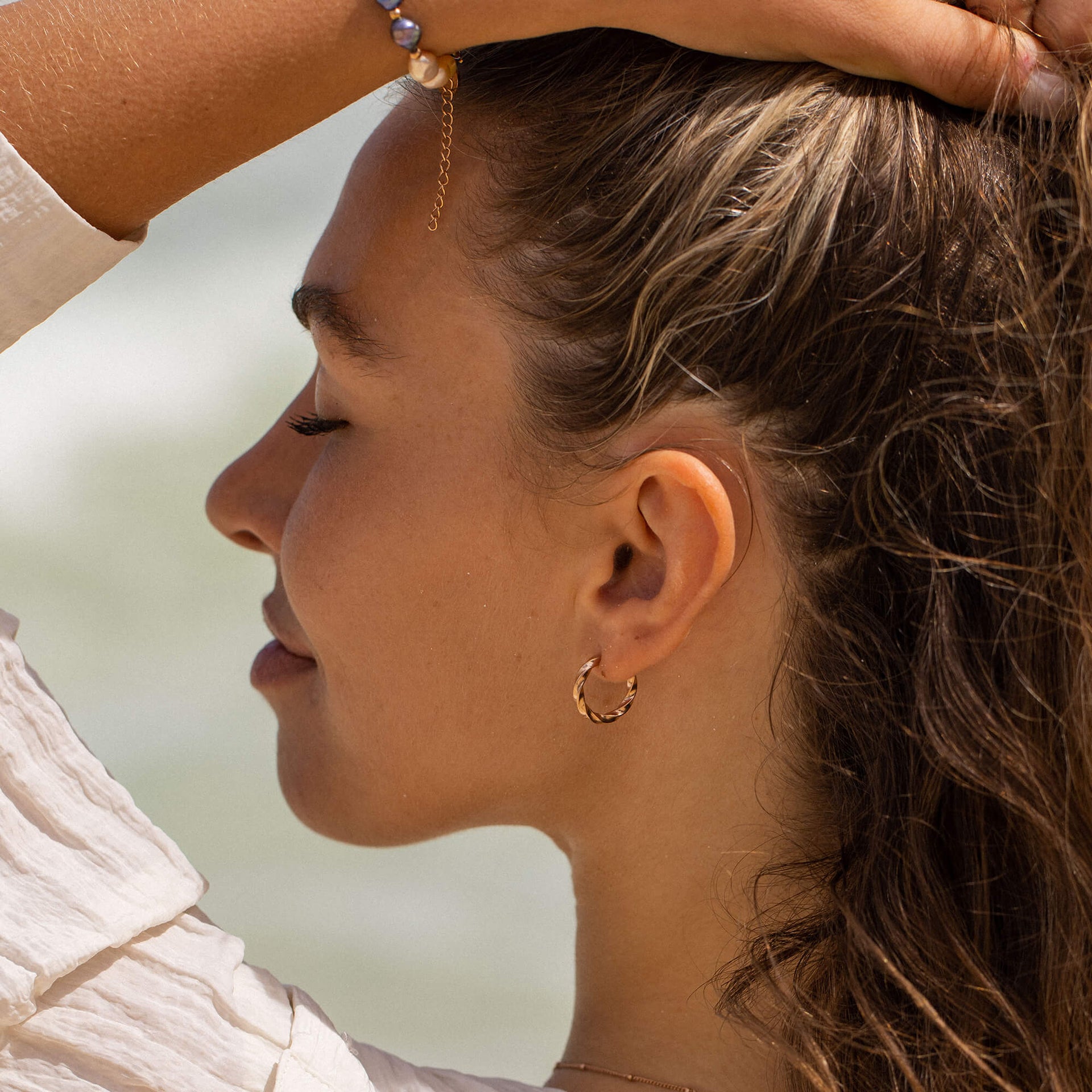 PURELEI Kelani Ohrringe aus goldfarbenem Edelstahl mit gewundenem Design, getragen im sanften Meereslicht.