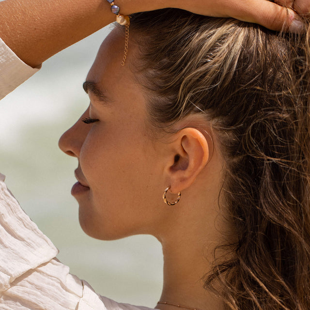 PURELEI Kelani Ohrringe aus goldfarbenem Edelstahl mit gewundenem Design, getragen im sanften Meereslicht.