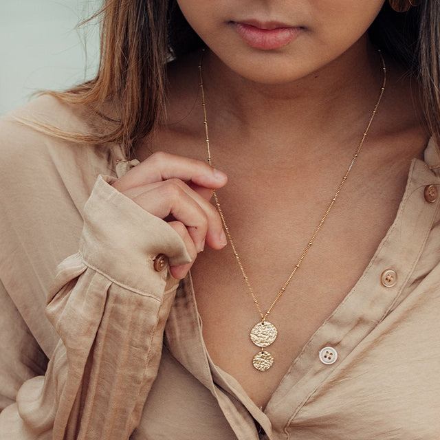 Malihini Coin Kette von PURELEI in 18K Gold, zwei strukturierte Anhänger, elegant getragen mit natürlichem Flair.