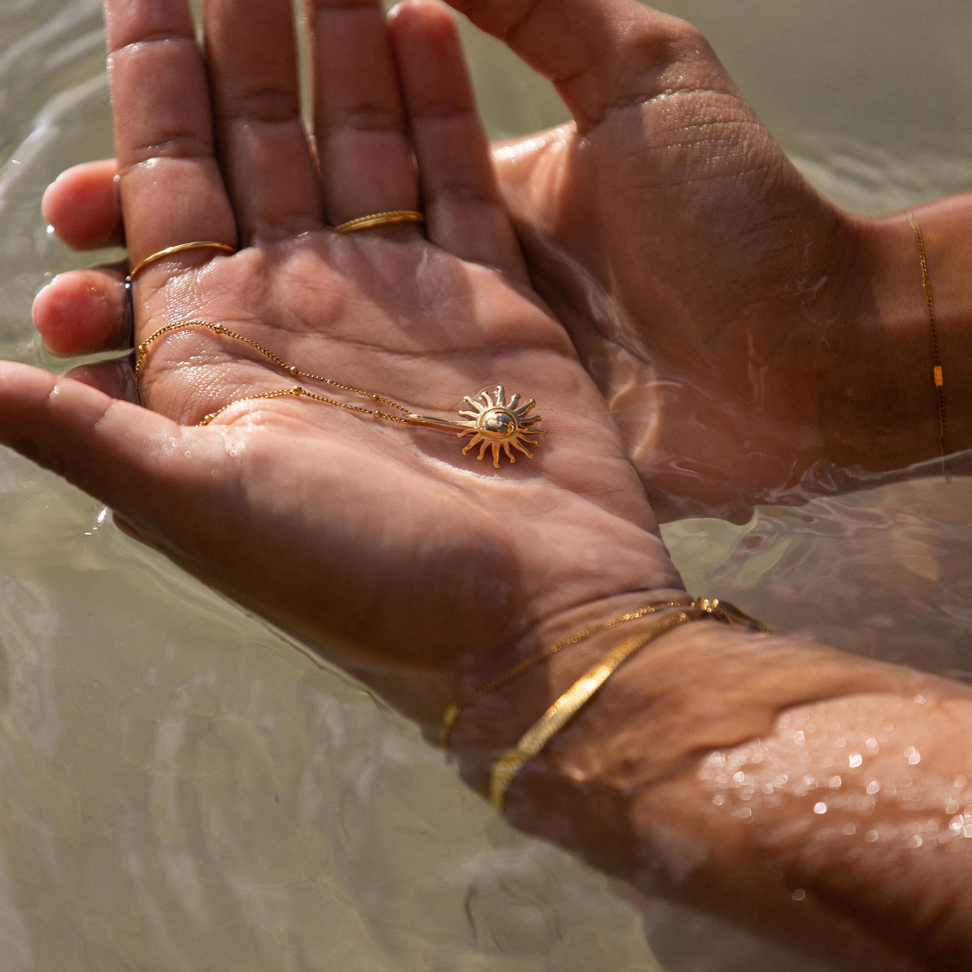 Sun Kette von PURELEI, goldene Edelstahlkette mit Sonnenanhänger, getragen im Wasser, strahlend und elegant.