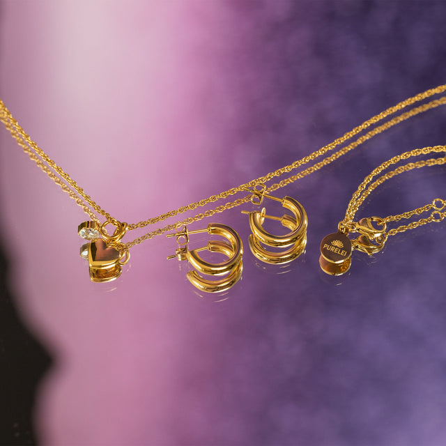 Goldene Kette und Creolen von PURELEI auf schimmerndem Hintergrund, elegant und modern.