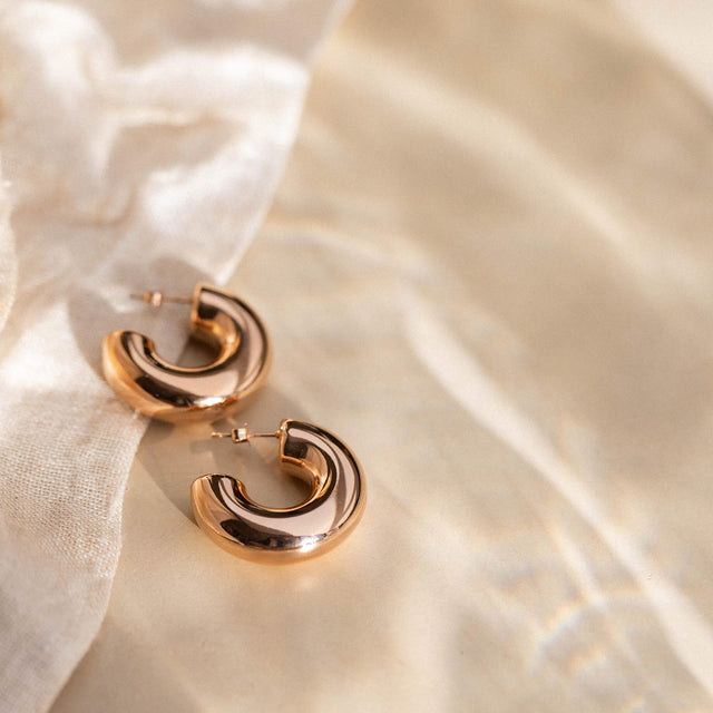 Roségoldene Creolen von PURELEI auf sanftem Stoff, elegant und modern.