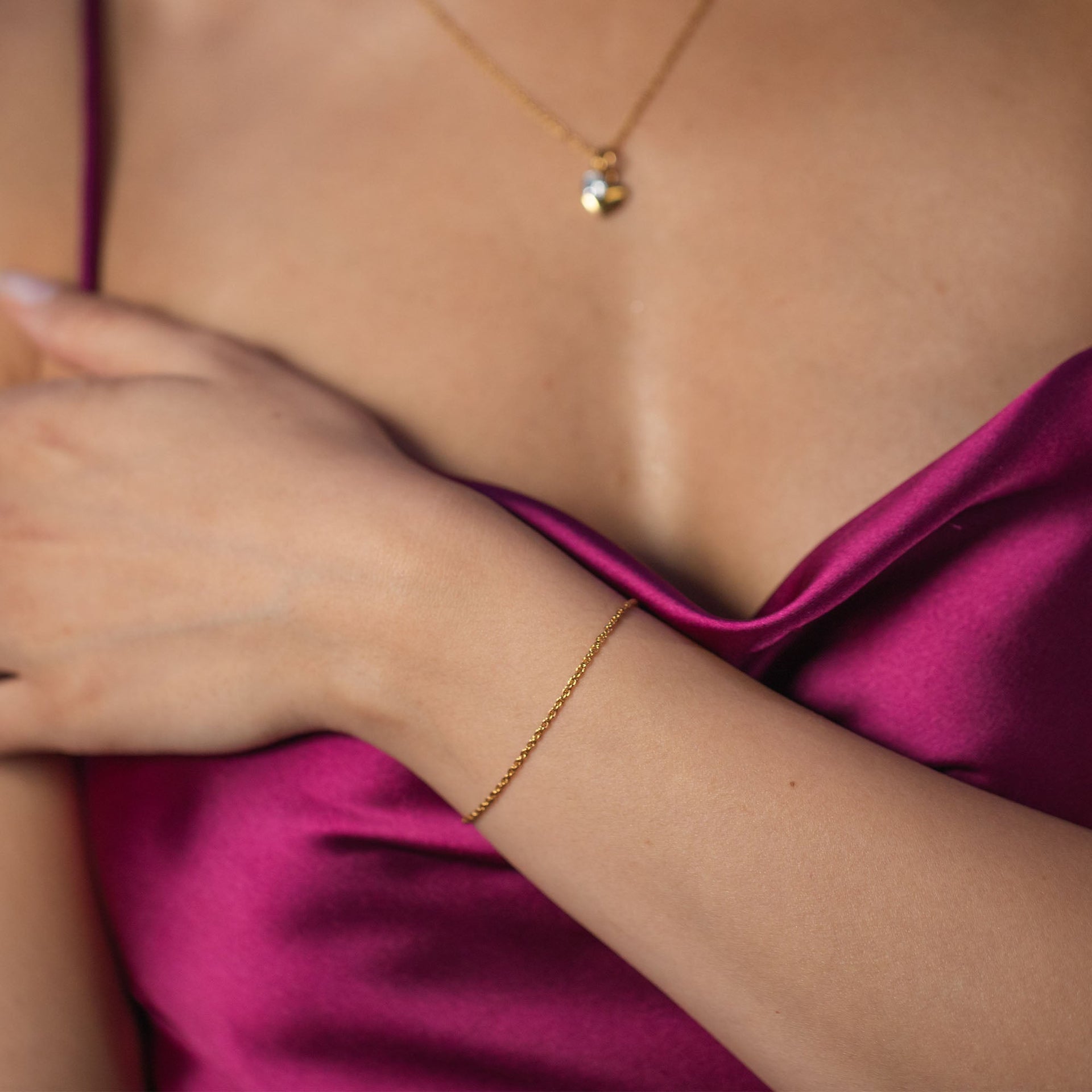 Zartes Roségold-Armband auf einem Handgelenk, getragen mit einem pinken Satinoberteil – PURELEI.