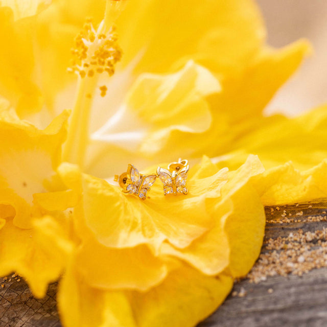 Goldene Schmetterling-Ohrstecker mit Glitzer auf gelber Blüte, PURELEI