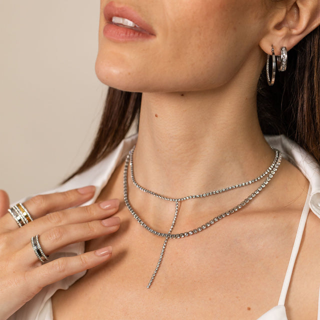 Silberne Kette mit funkelnden Details, getragen mit Ringen und Ohrringen von PURELEI.