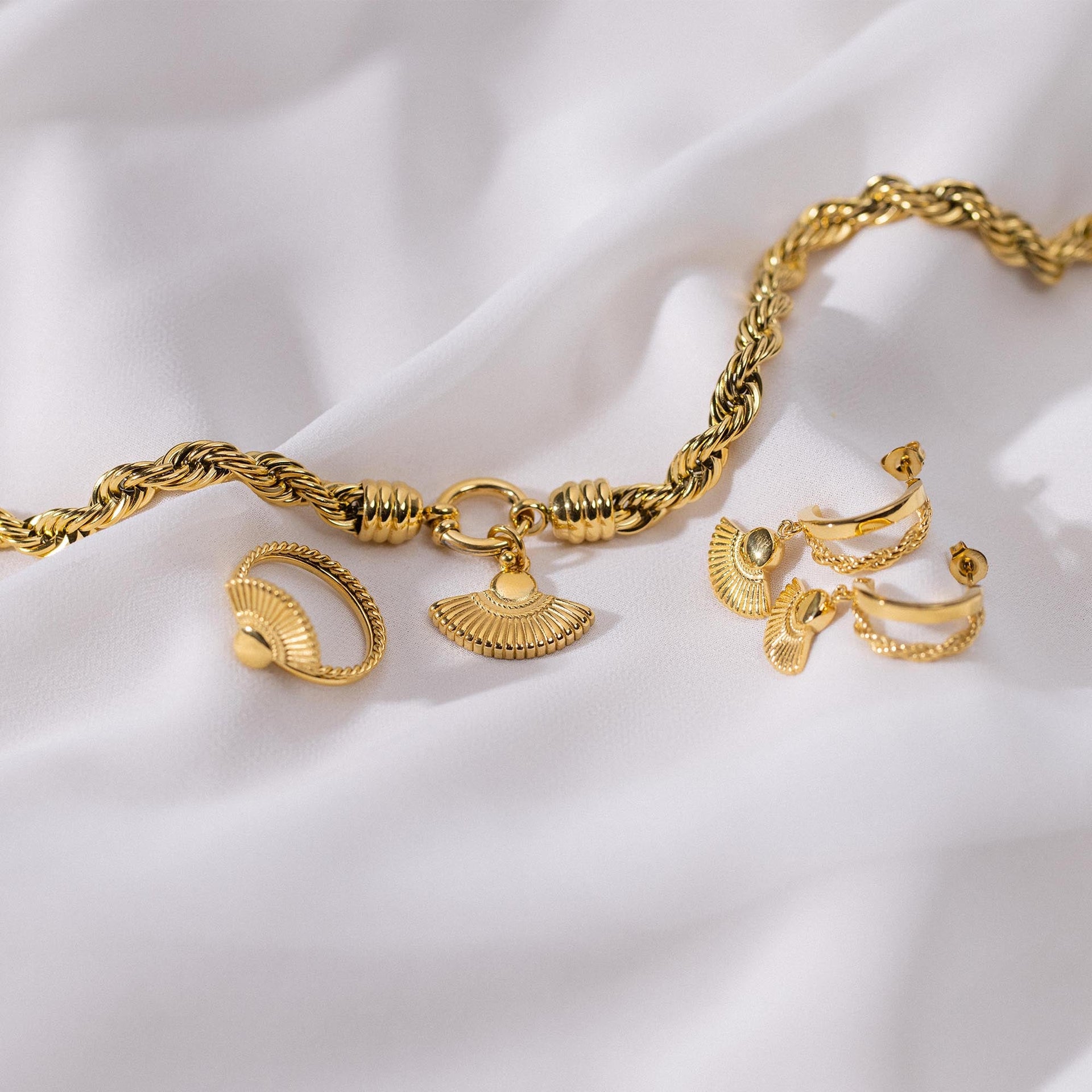 PURELEI Breeze Charm Anhänger in 18K Gold mit Fächerdesign, auf edlem weißen Stoff inszeniert.