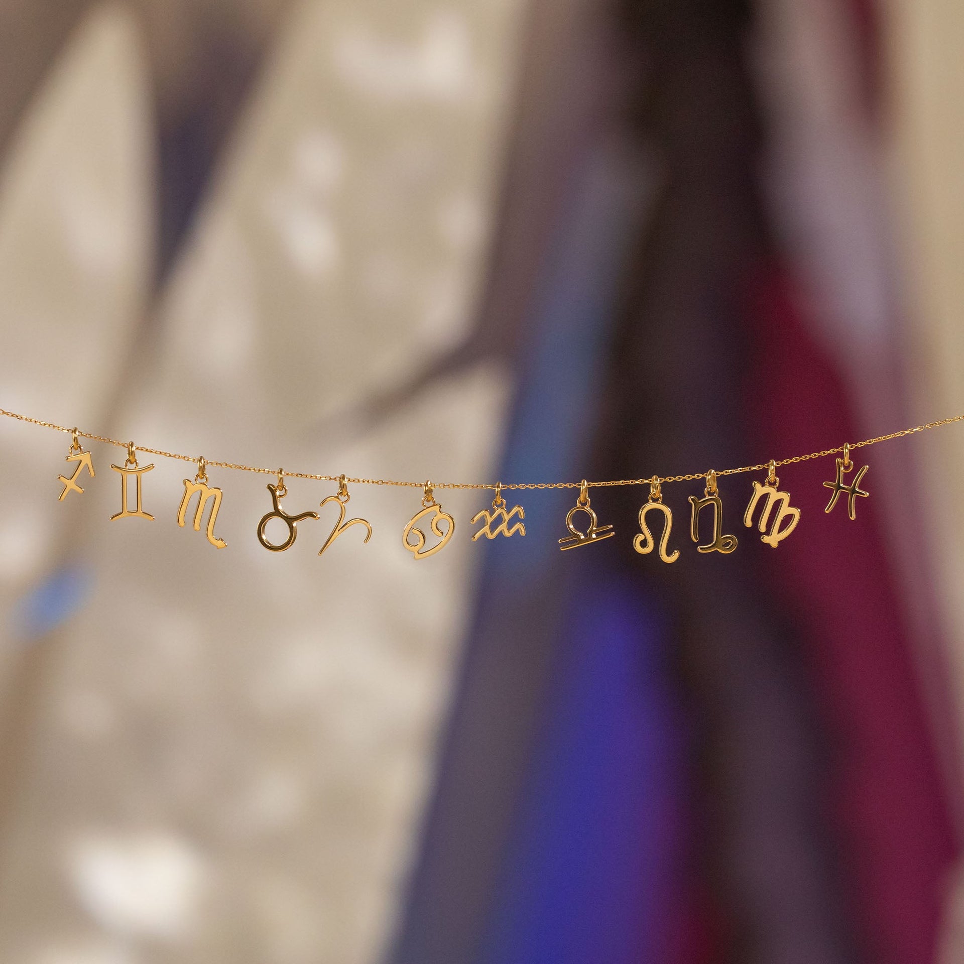 PURELEI Wassermann Zodiac Charm in 18K Gold, filigran und nickelfrei, schwebend vor sanft verschwommenem Hintergrund